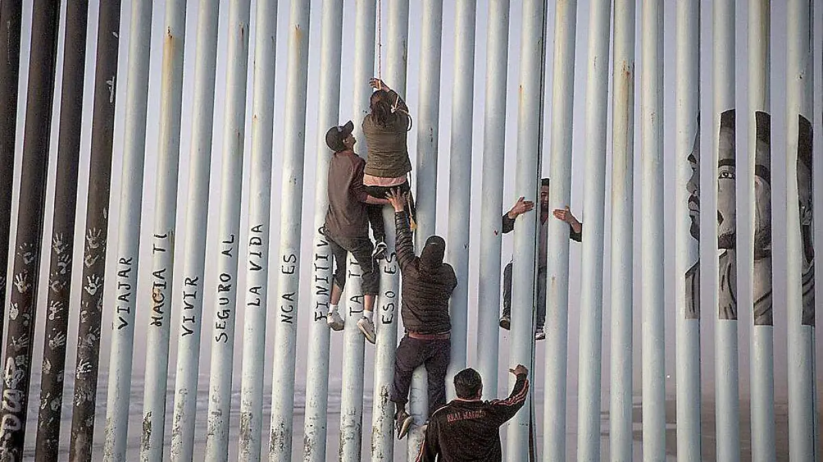 Migrantes cruzando el muro fronterizo